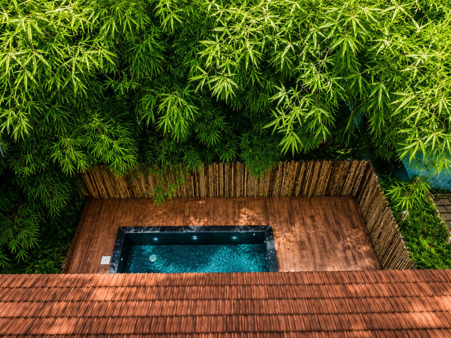 Un jacuzzi rodeado de follaje de bambú y una terraza de madera.