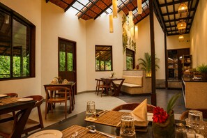 A dining area with tables set for two, wooden chairs, and a sofa.