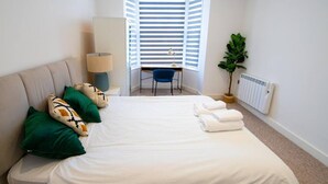 A bedroom with a bed, pillows, a desk, a chair, a lamp, a radiator, and a plant. - Little Haven - apartment in Rye (East Sussex)