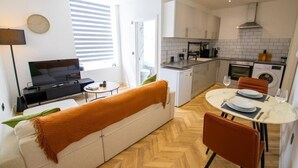 A modern apartment with a living room, dining area, kitchenette, and a large window. - Little Haven - apartment in Rye (East Sussex)