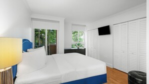 A bedroom with a bed, a TV mounted on the wall, and a window with a view of greenery. - Modern 2BR Grove Condo w/ King & Balcony (Miami)