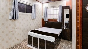 A bedroom with a bed, a window with curtains, a ceiling fan, and a mirror. - Deluxe Hotel Garden Inn (Ambernath)