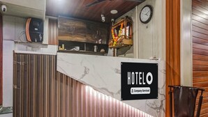 A hotel reception desk with a 'HOTELO' sign, a clock, and a wooden panel wall. - Deluxe Hotel Garden Inn (Ambernath)