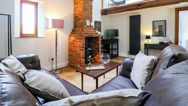 Una sala de estar con chimenea de ladrillo, sofá de cuero y una mesa de comedor.