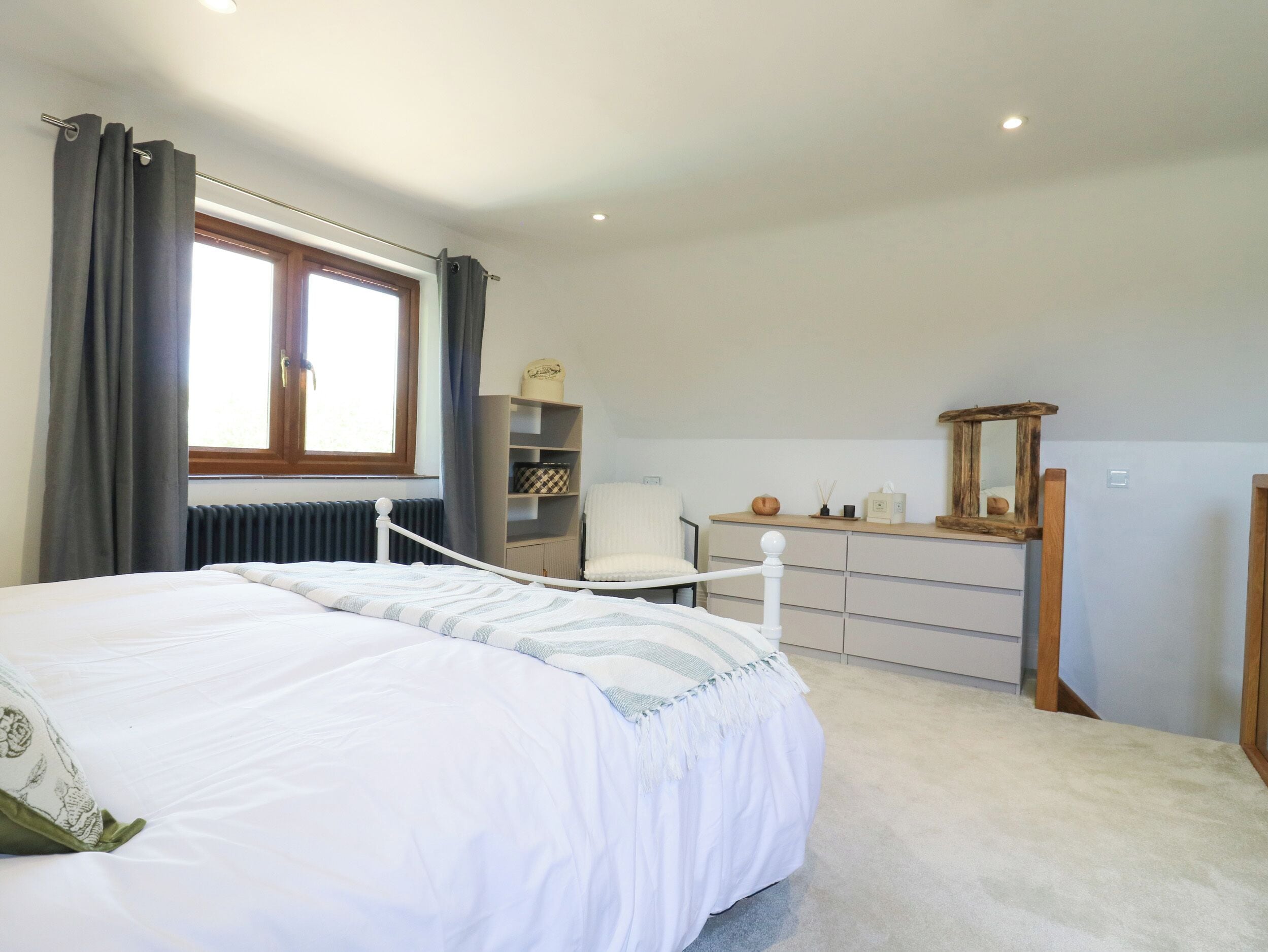 Un dormitorio con cama, cómoda, espejo, radiador y ventana con cortinas.