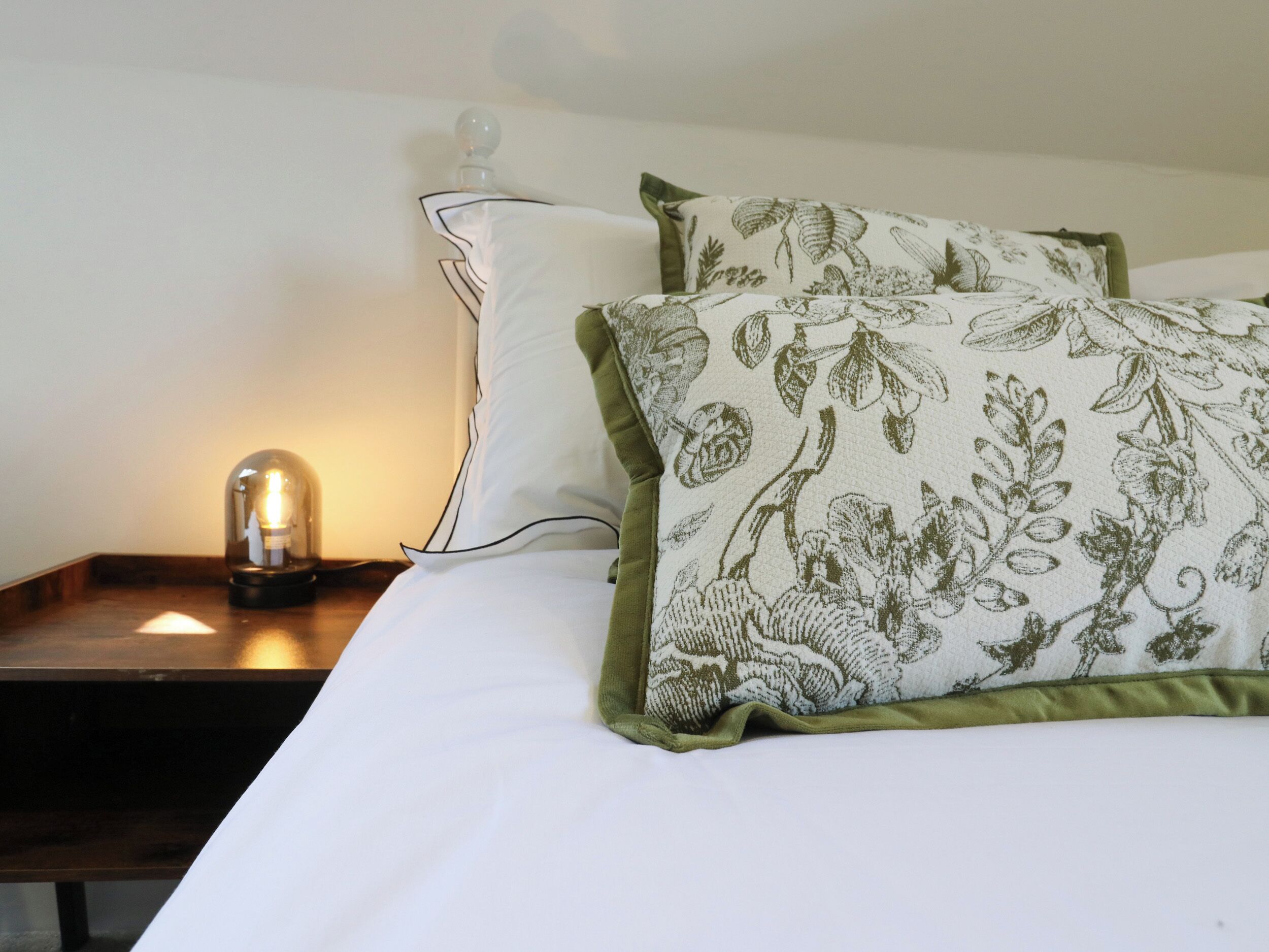 A bed with white bedding and two pillows, one with a floral pattern and the other plain.