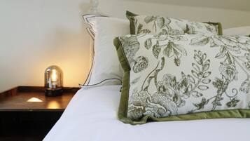 A bed with white bedding and two pillows, one with a floral pattern and the other plain.