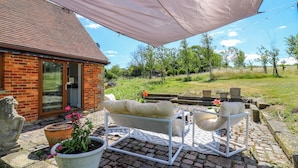 Un patio con un sofá y sillas blancos para exteriores, un paraguas grande y una casa de ladrillo con puerta de cristal.