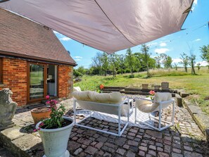 Un patio con un sofá y sillas blancos para exteriores, un paraguas grande y una casa de ladrillo con puerta de cristal.