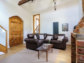 Una sala de estar con un sofá de cuero marrón, una mesa de centro de madera, una puerta grande de madera y una pared de ladrillo.