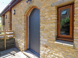 A stone building with a wooden door, a window with a wooden frame, and a wooden bench outside.