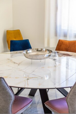 A round marble table with a metallic bowl in the center, surrounded by chairs with cushioned seats.
