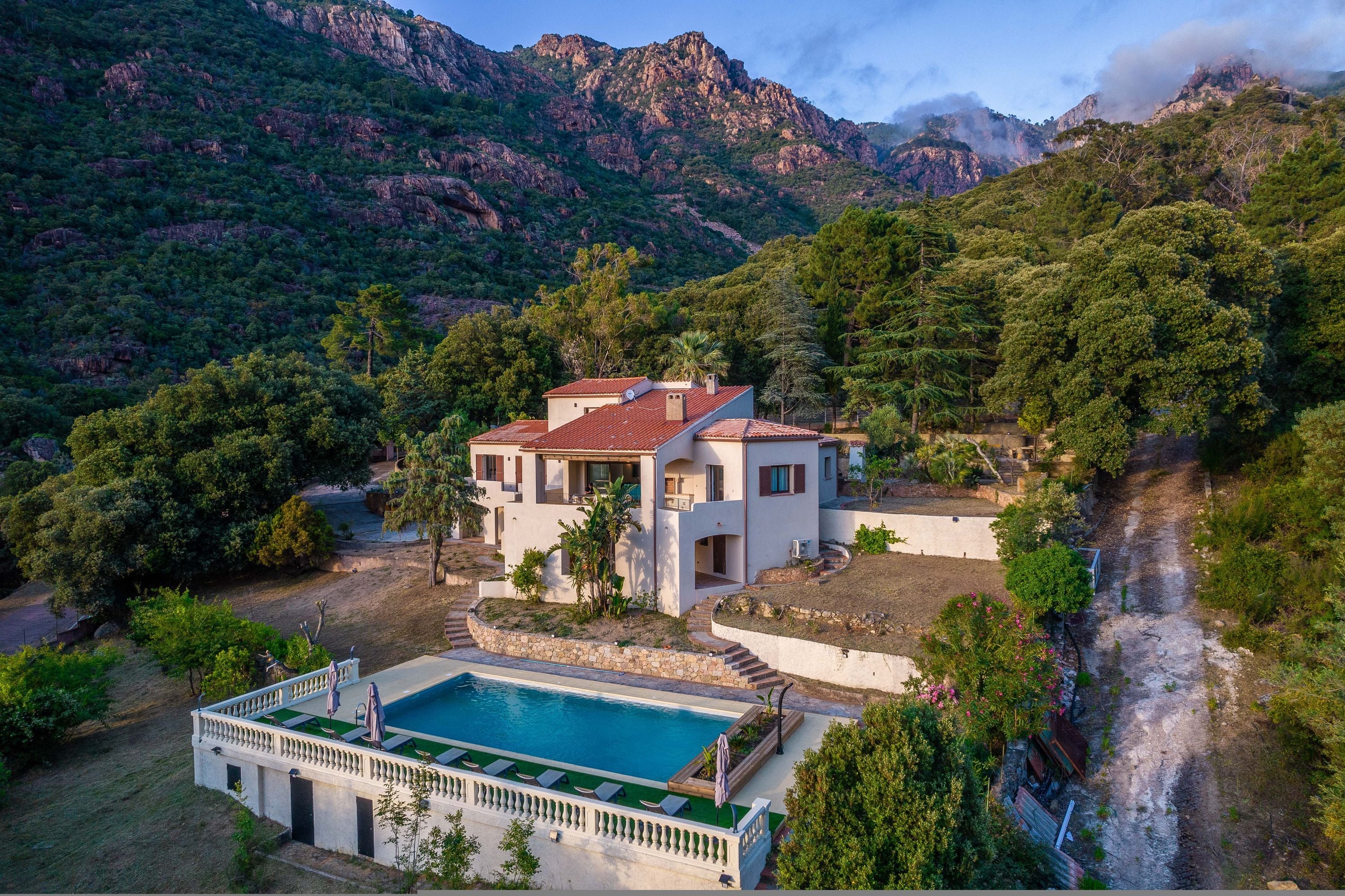 Una villa con piscina, rodeada de exuberante vegetación y montañas.