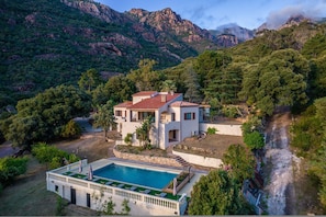 A villa with a swimming pool, surrounded by lush greenery and mountains.