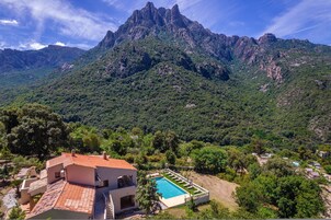 Una villa con piscina, rodeada de exuberante vegetación y montañas.