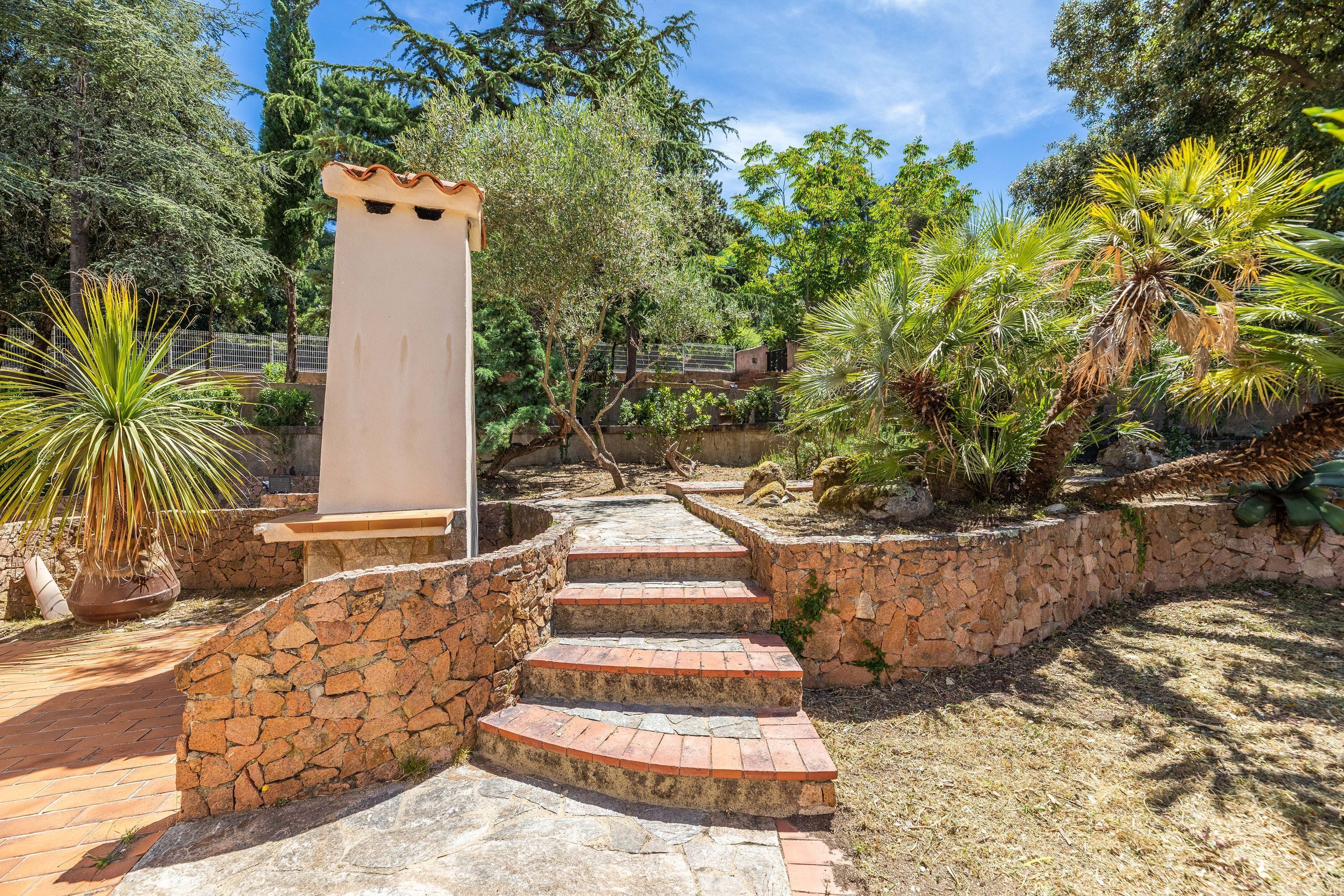 A stone staircase leading to a white structure, surrounded by lush greenery and a stone wall.