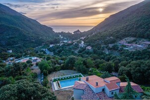 Paisaje montañoso con piscina, casas y una carretera.