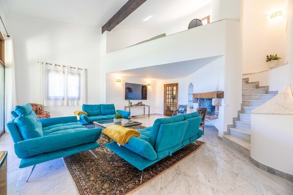 A spacious living room with a high ceiling, a staircase, and a fireplace.
