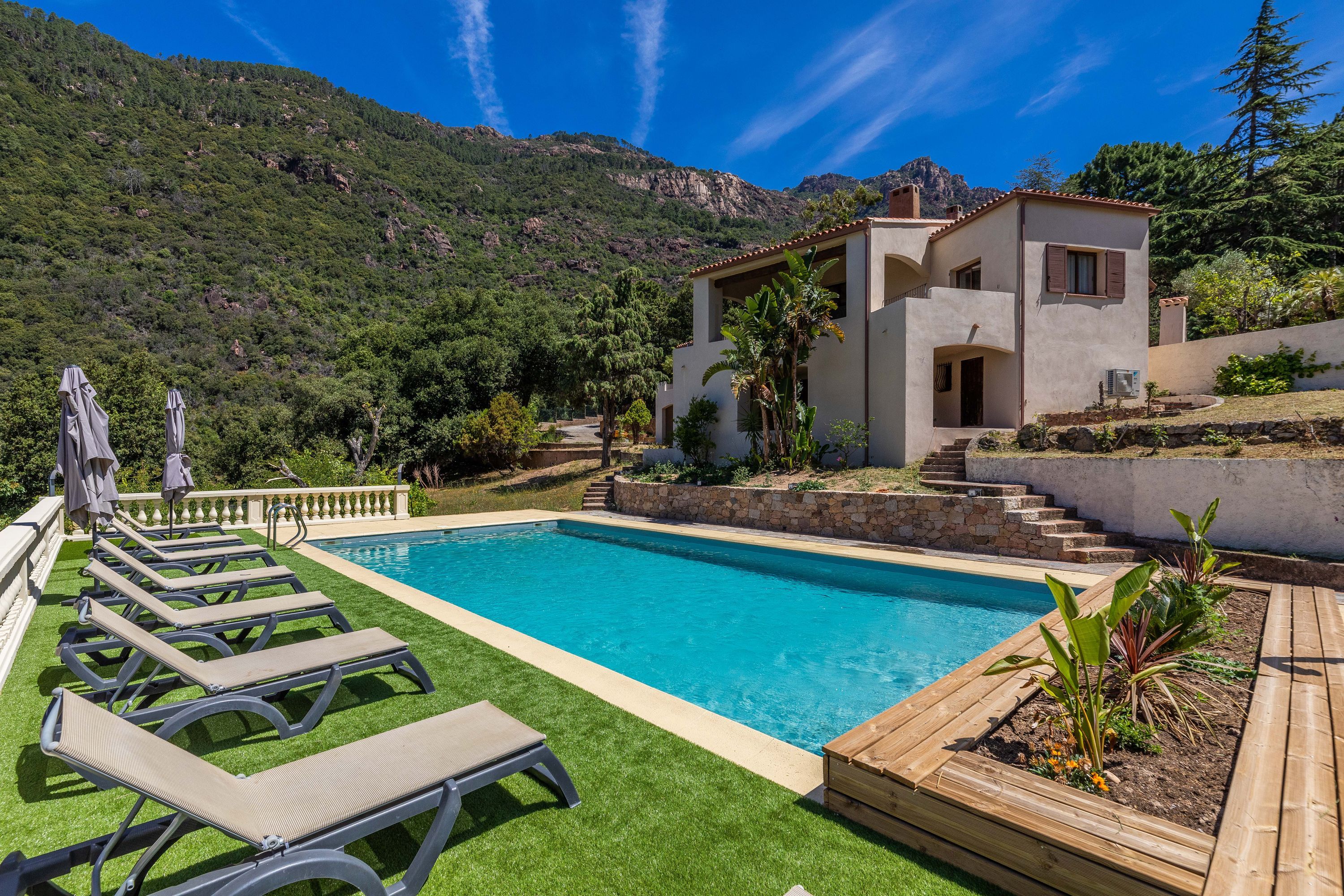 A swimming pool with lounge chairs, a stone building, and a mountainous backdrop.