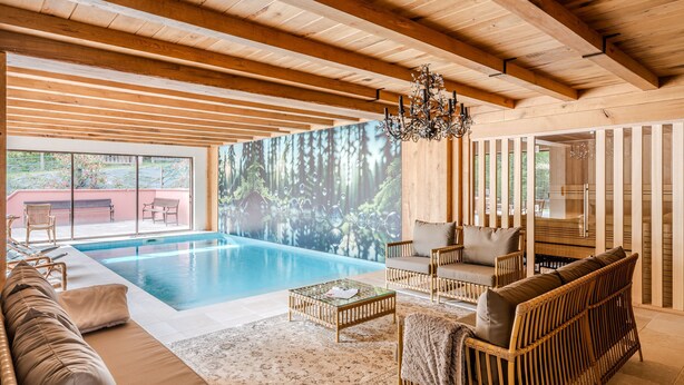 A spacious indoor pool area with a wooden ceiling, a large wall mural, and a comfortable seating area with a sofa and chairs. - Le Buchwald in Dambach (Dambach)