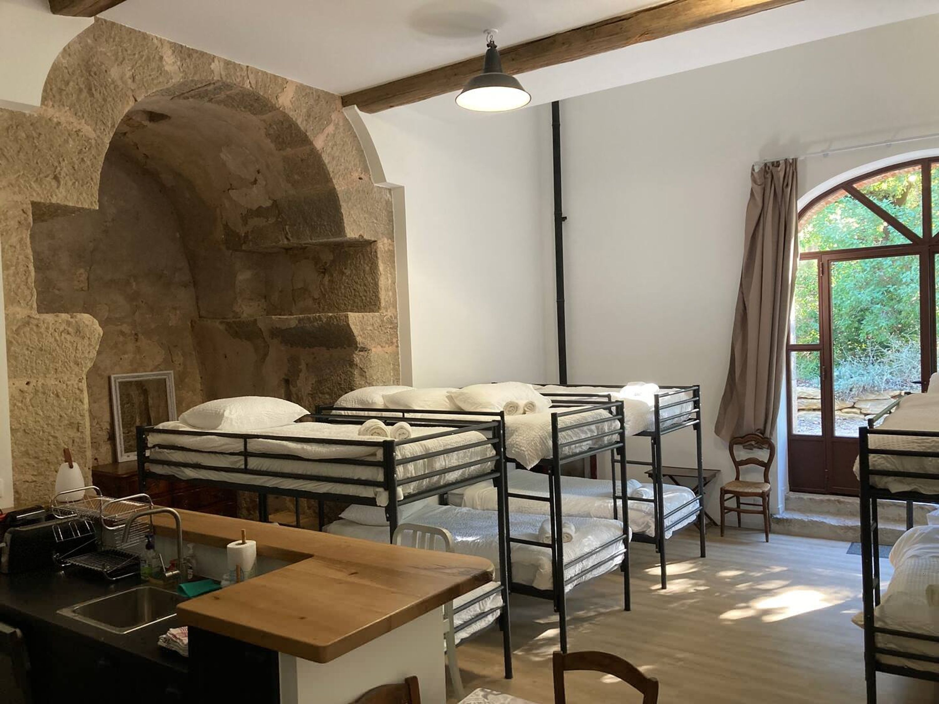 Bunk beds with white bedding, a wooden desk, a sink, and a stone archway.