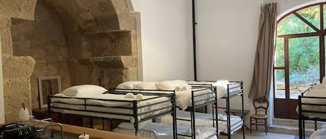 Bunk beds with white bedding, a wooden desk, a sink, and a stone archway.