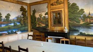 Ein Esszimmer mit einem langen Tisch, Stühlen, einer Chandelier und Wandmalereien.