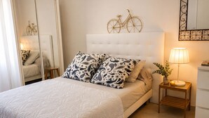A bedroom with a bed, a bedside table with a lamp, a mirror, and a decorative bicycle wall art. - Bas de Villa Lola Avec Piscine (Six-Fours-les-Plages)