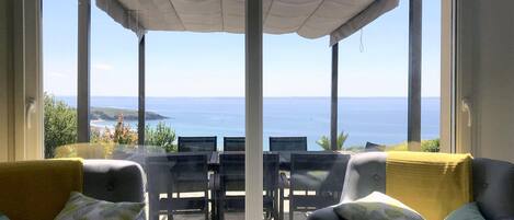 A balcony with a view of the sea, a pergola, and two sofas with cushions.