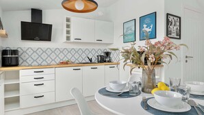 A modern kitchen with white cabinets, a black range hood, a wooden countertop, and a dining table set with white plates and bowls. - Comfortable Apartment with Parking | Close to the Beach (Dziwnówek)