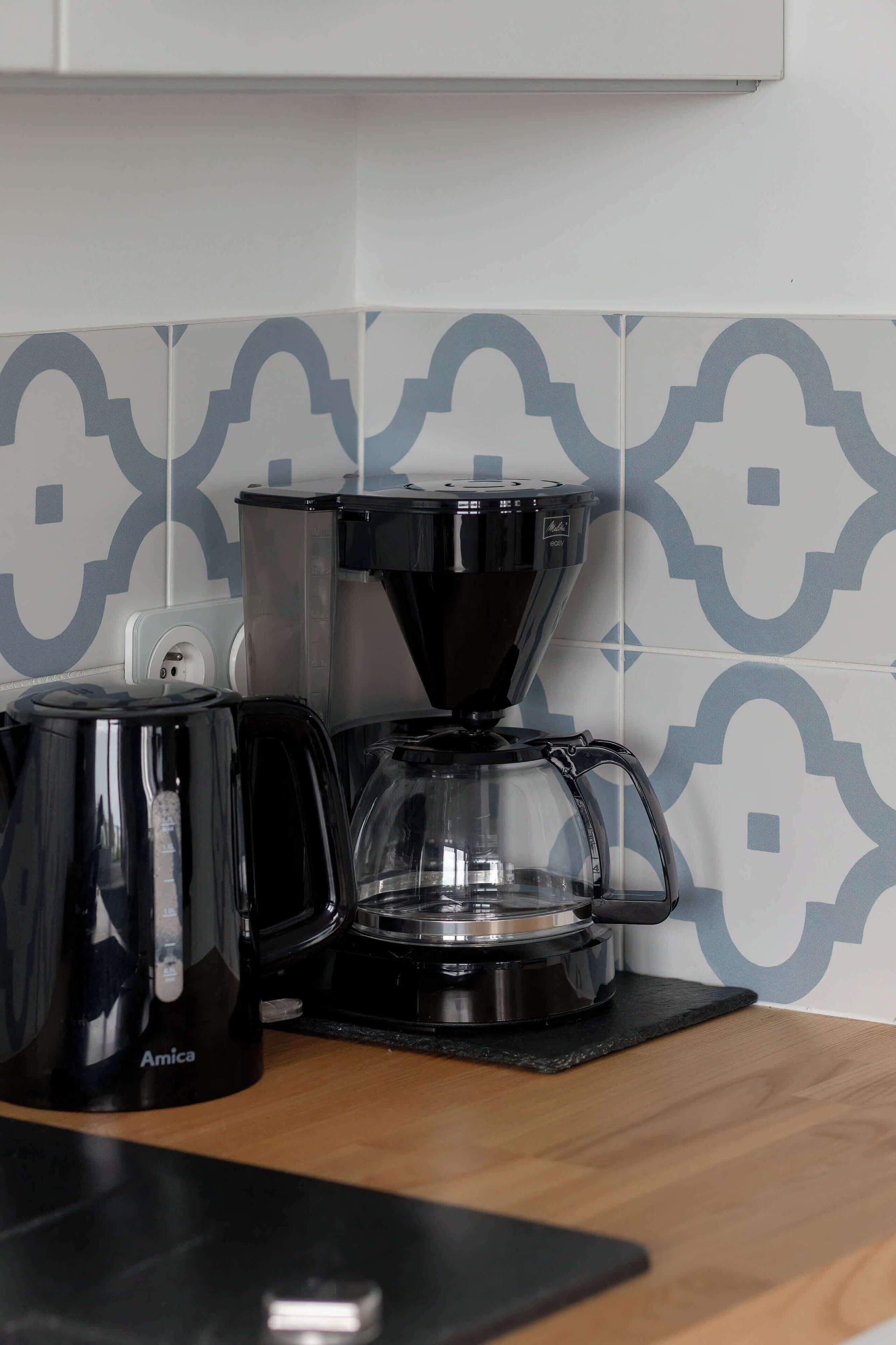 A coffee maker and a kettle on a countertop with a patterned backsplash.