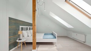 A bedroom with a sloped ceiling, a bed, a small table with a lamp, and a radiator. - Comfortable Apartment with Parking | Close to the Beach (Dziwnówek)