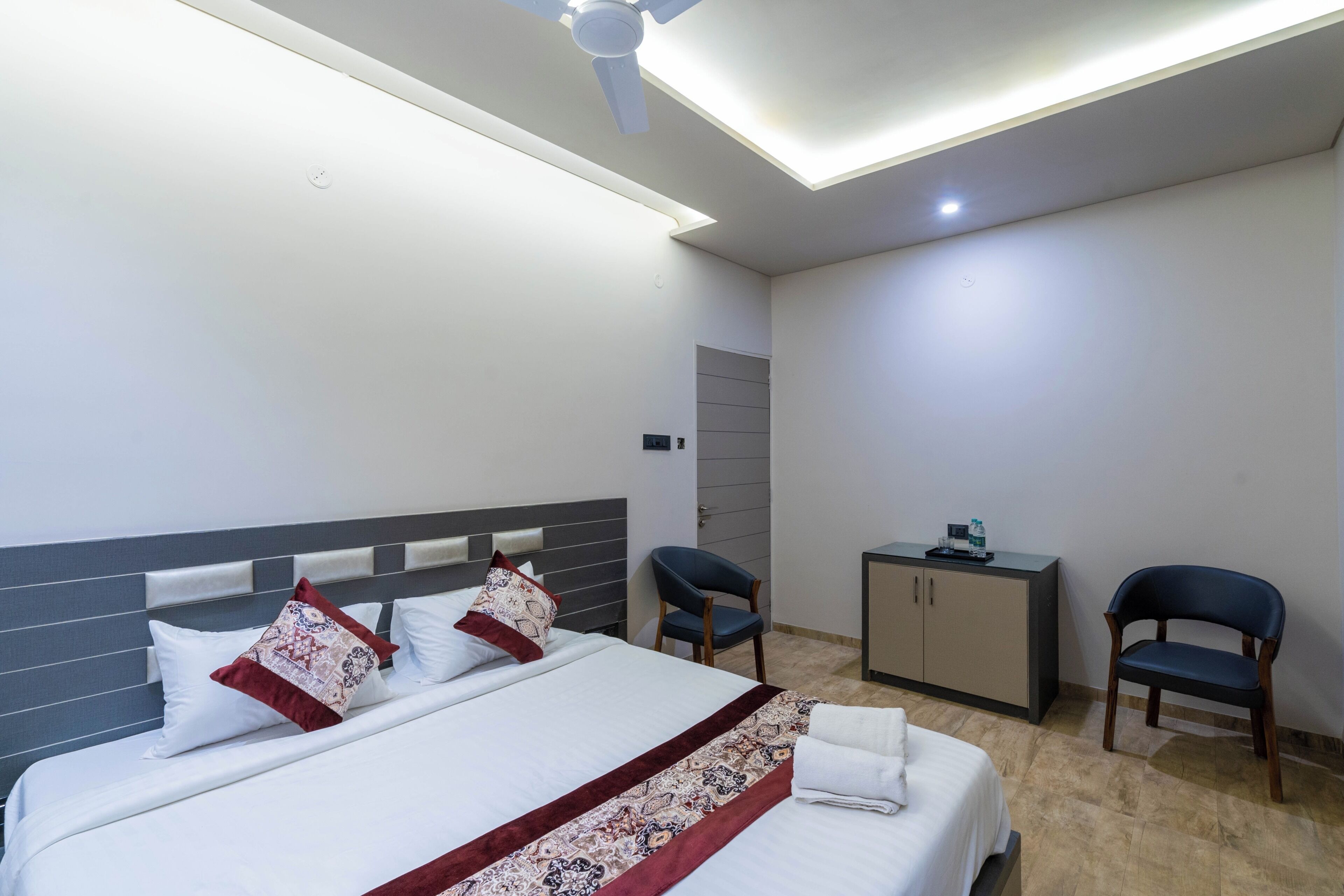 A hotel room with a bed, two chairs, a desk, and a ceiling fan.