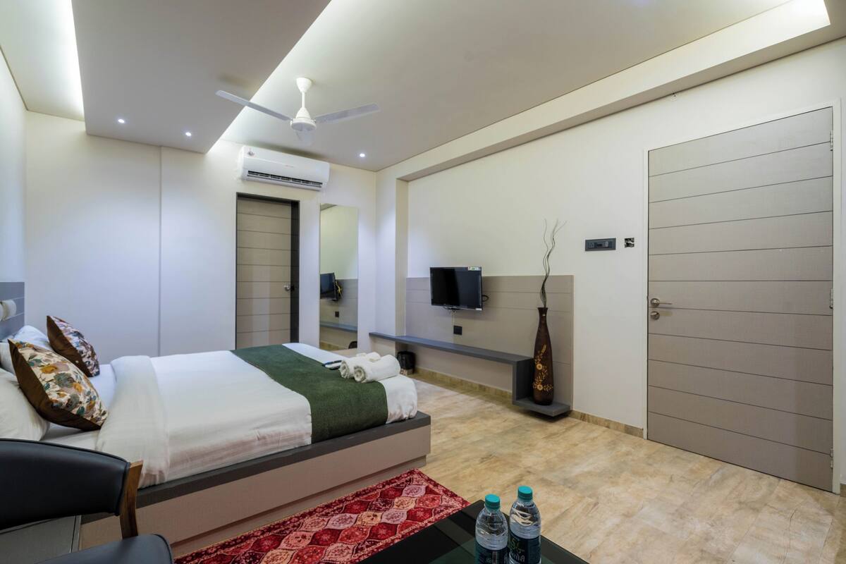 Una habitación de hotel moderna con cama, televisor de pantalla plana, ventilador de techo, aire acondicionado, armario grande y alfombra roja con diseño.
