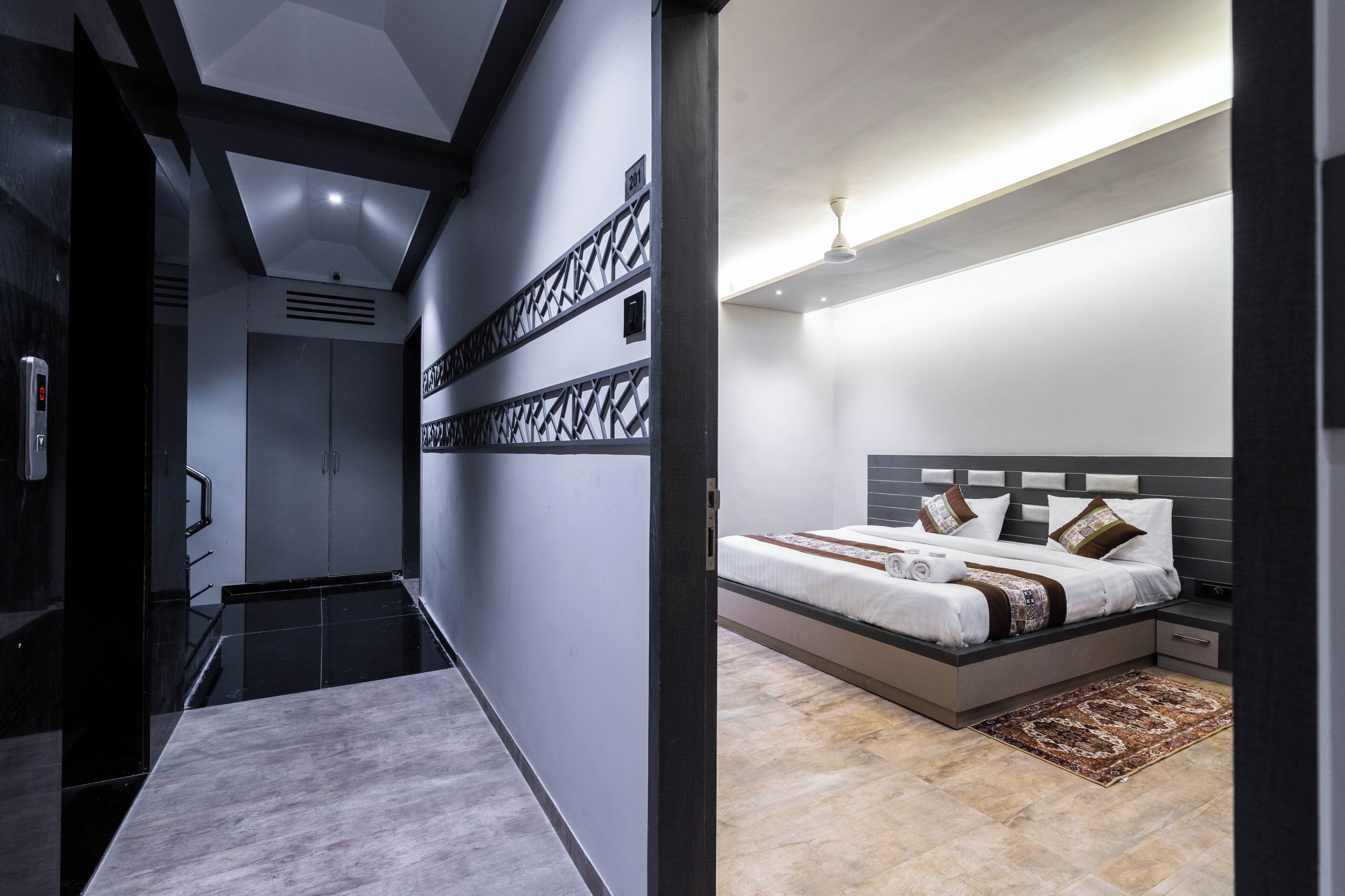 A modern hotel room with a large bed, a nightstand, a desk, and a bathroom with a shower and toilet.