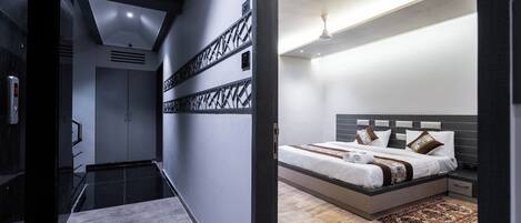 A modern hotel room with a large bed, a nightstand, a desk, and a bathroom with a shower and toilet.
