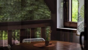 An indoor seating area with a round table, chairs, and a window with a view of greenery.