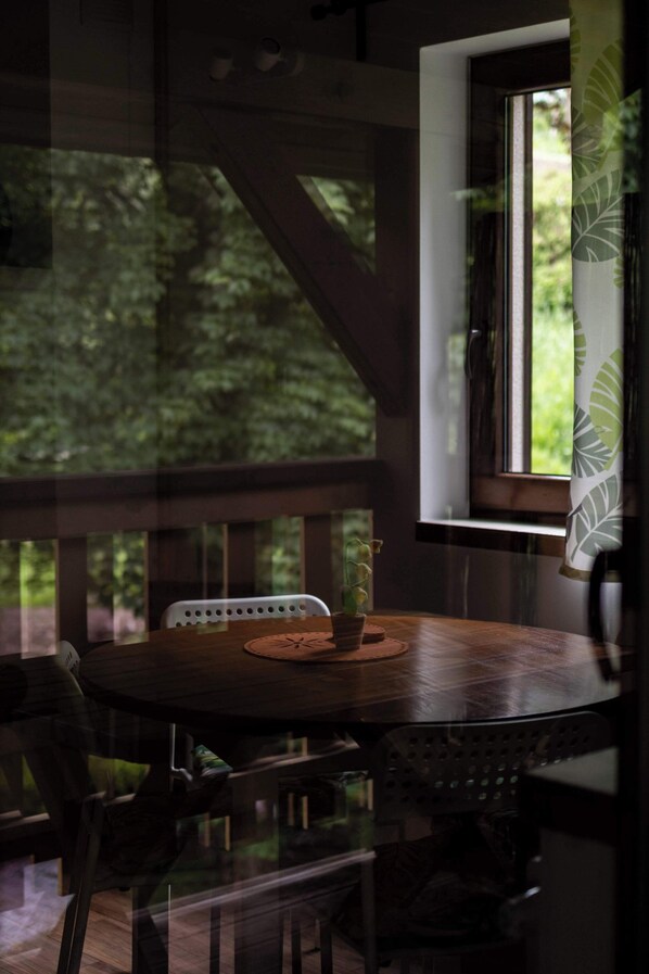 An indoor seating area with a round table, chairs, and a window with a view of greenery.