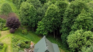 A house surrounded by dense trees, with a visible chimney and a small porch area.