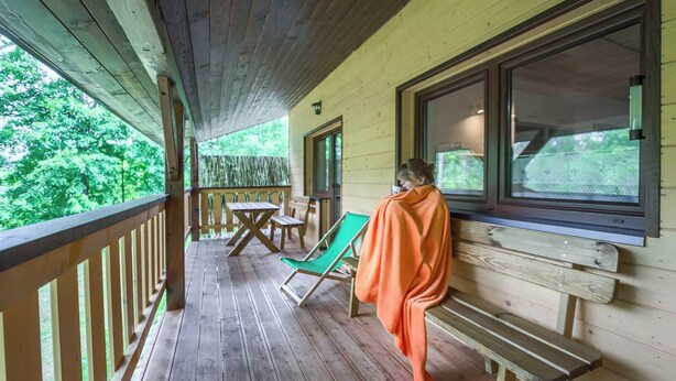 A wooden deck with a table and chairs, a bench, and a person sitting by a window.