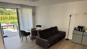 A modern living room with a sofa, a dining table with chairs, a coffee station, and a view of a garden through a glass door. - Modern Vacation Rental Near Phandtasialand: A Short Getaway 2 (Weilerswist)