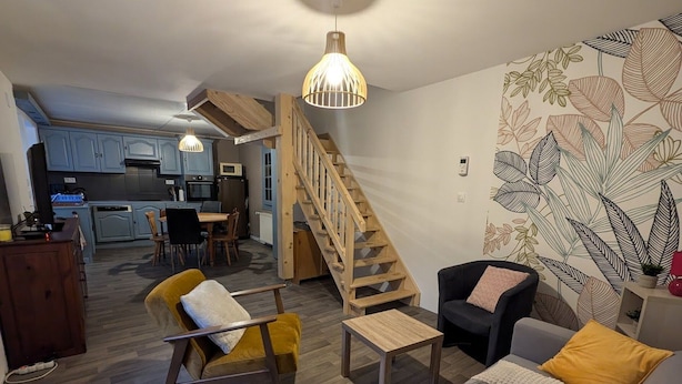 Ein modernes Wohnzimmer mit Sofa, Sessel und Couchtisch, einer Treppe und einer Küche im Hintergrund.