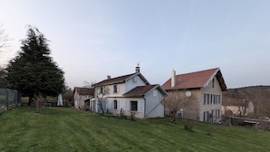 Ein zweistöckiges Haus mit einem geneigten Dach, einem umzäunten Garten und einem großen Baum.