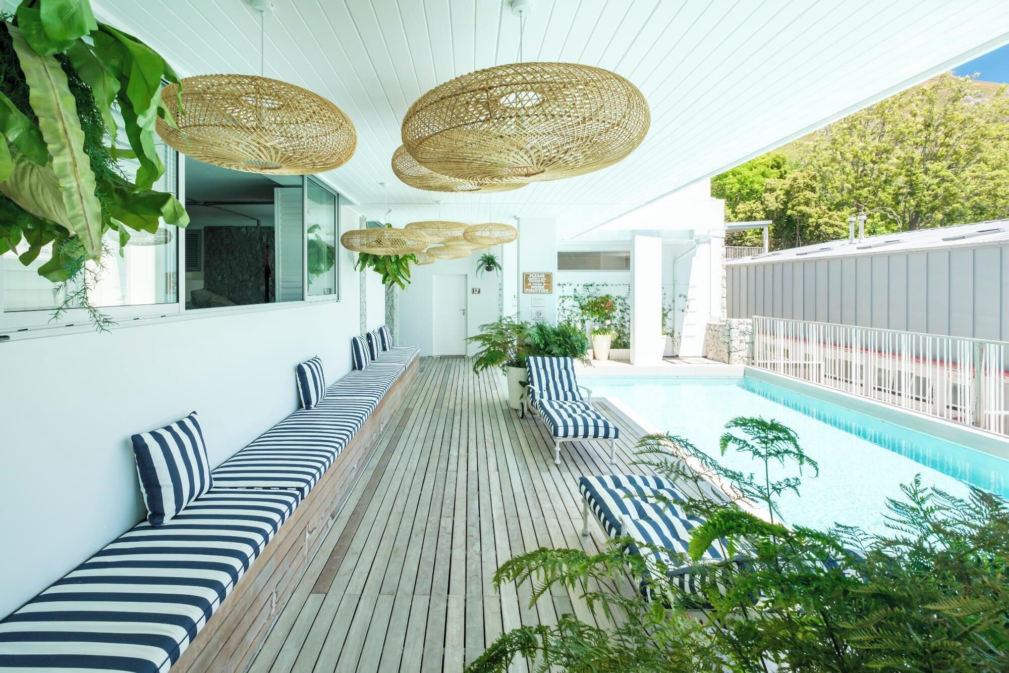 A poolside area with a wooden deck, striped seating, and hanging rattan lamps.