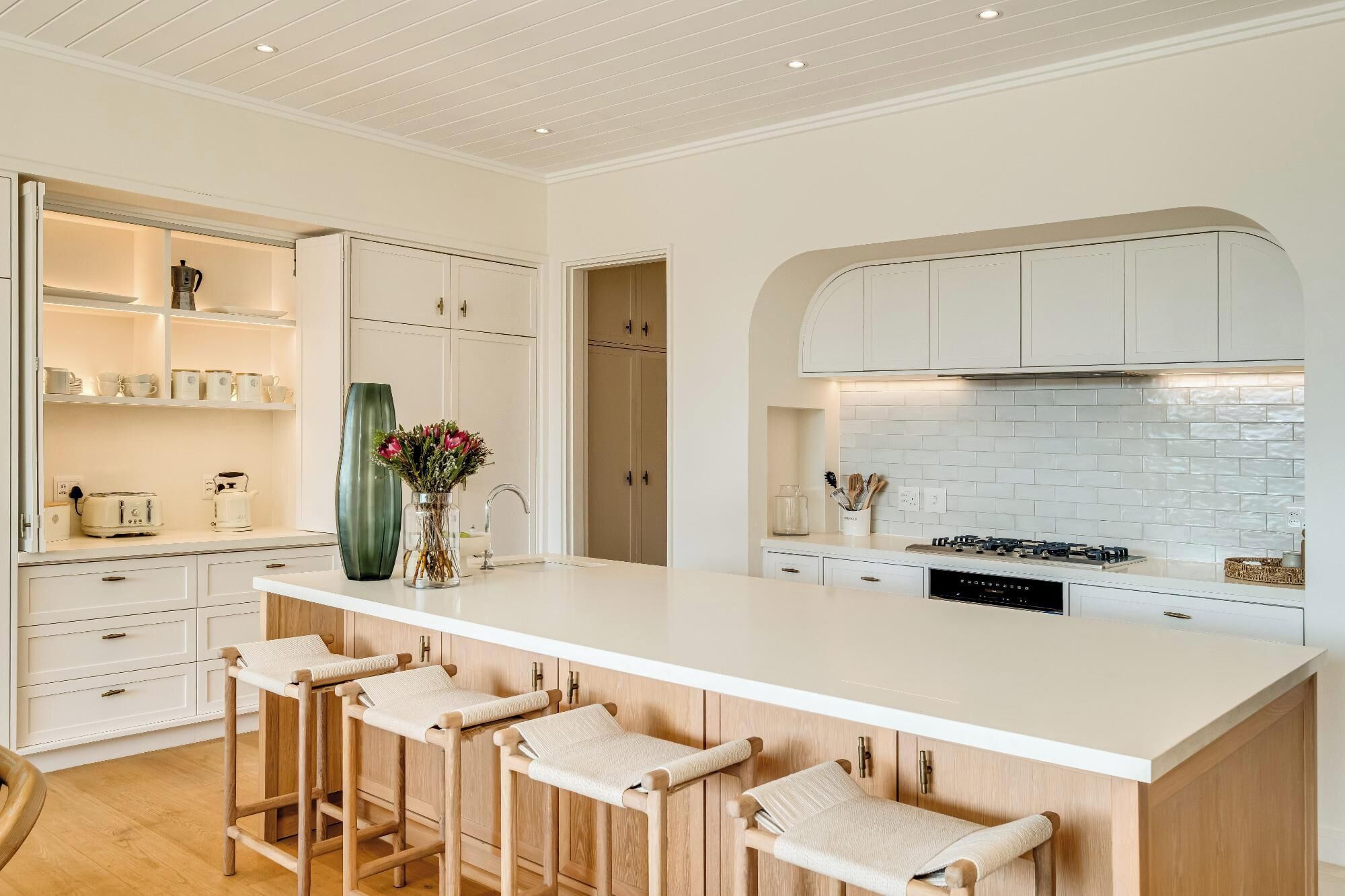 Una cocina moderna con armarios blancos, una isla central con taburetes y un salpicadero de ladrillo.