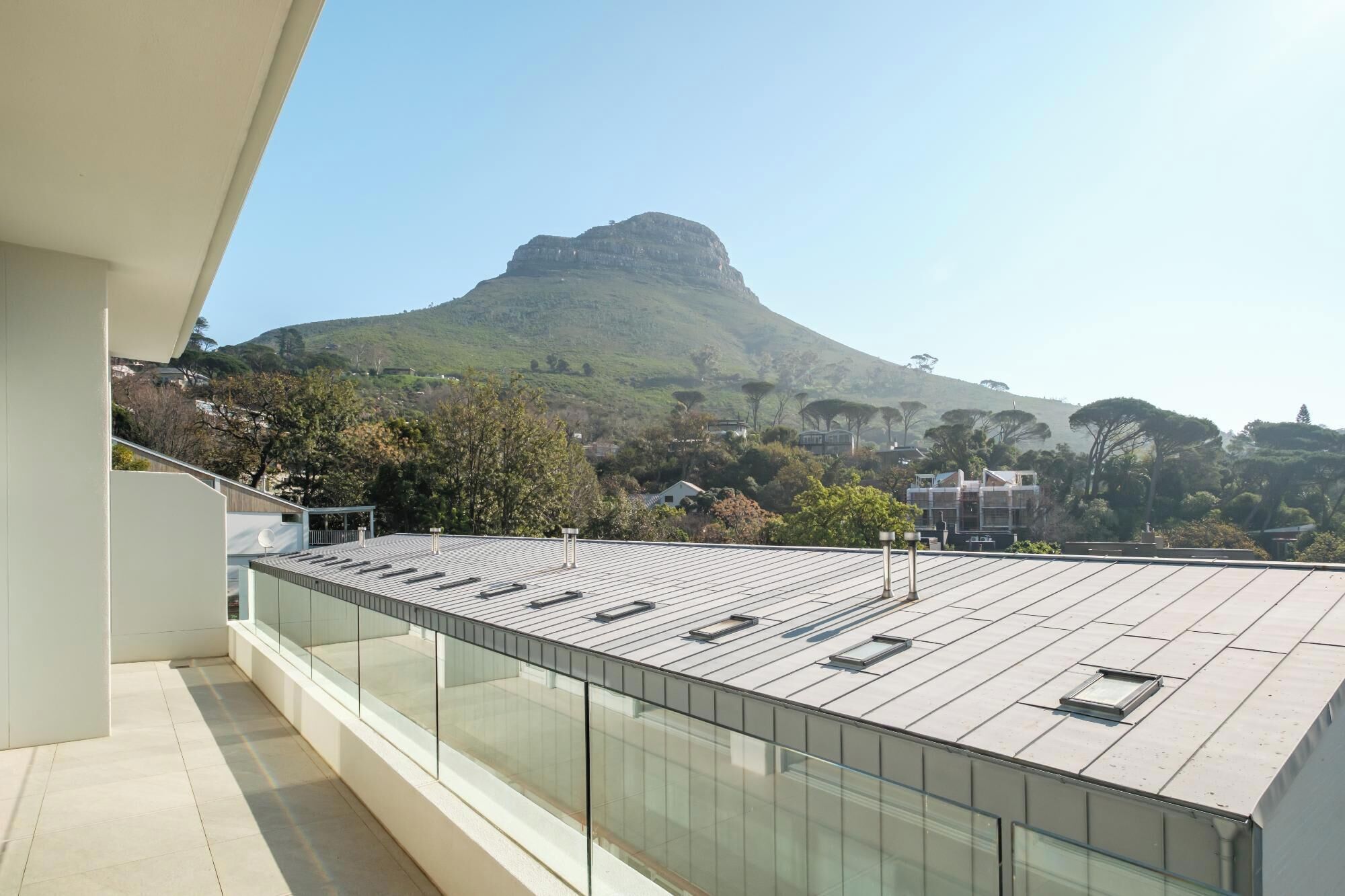 A modern building with a flat roof, large windows, and a view of a hill.
