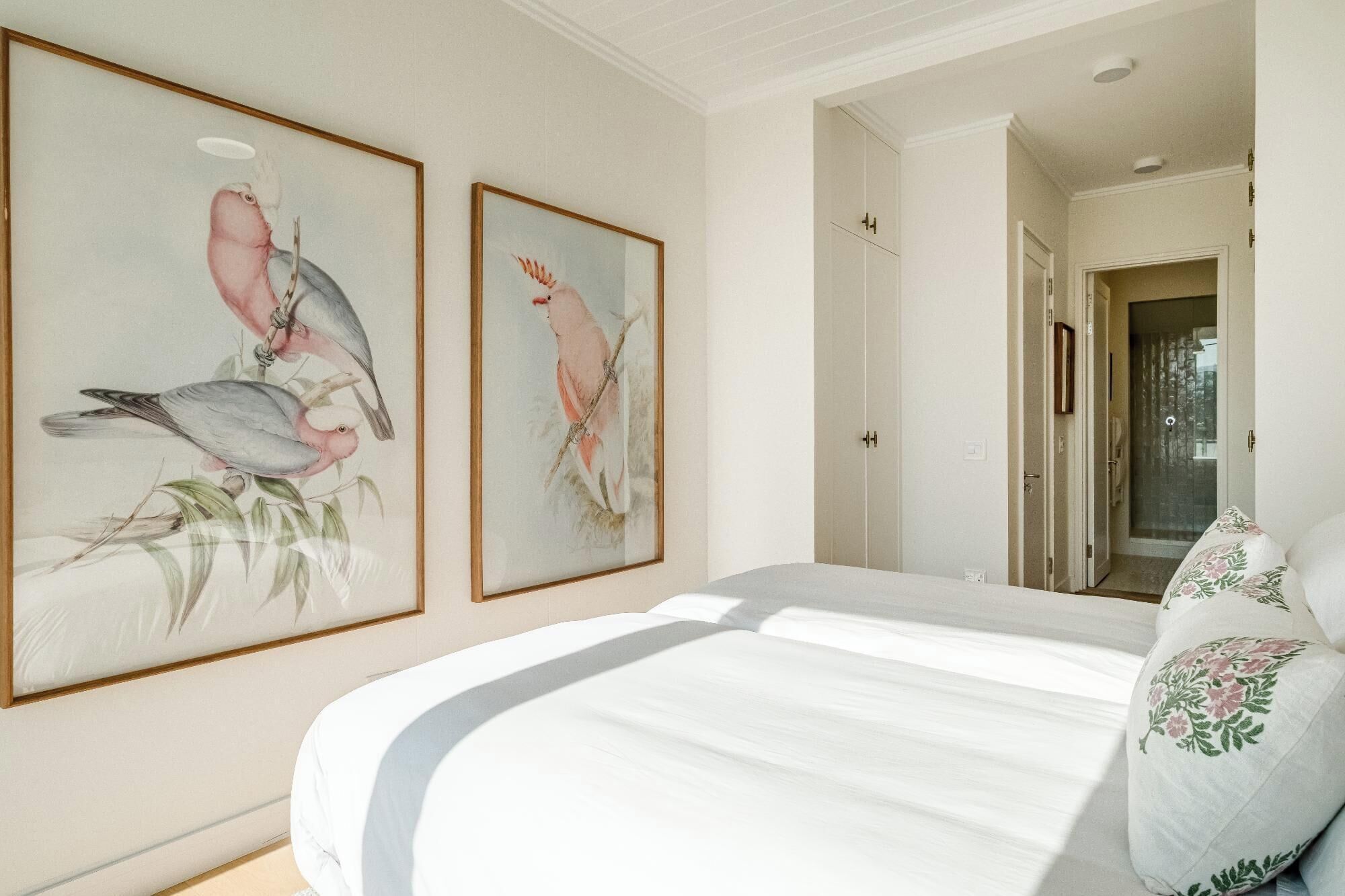 A bedroom with a bed, two framed wall art pieces, a door, and a shower area.