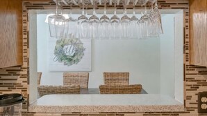 Eine Küche mit Arbeitsplatte, hängenden Weingläsern, Korbstühlen und einer Wandleuchte.