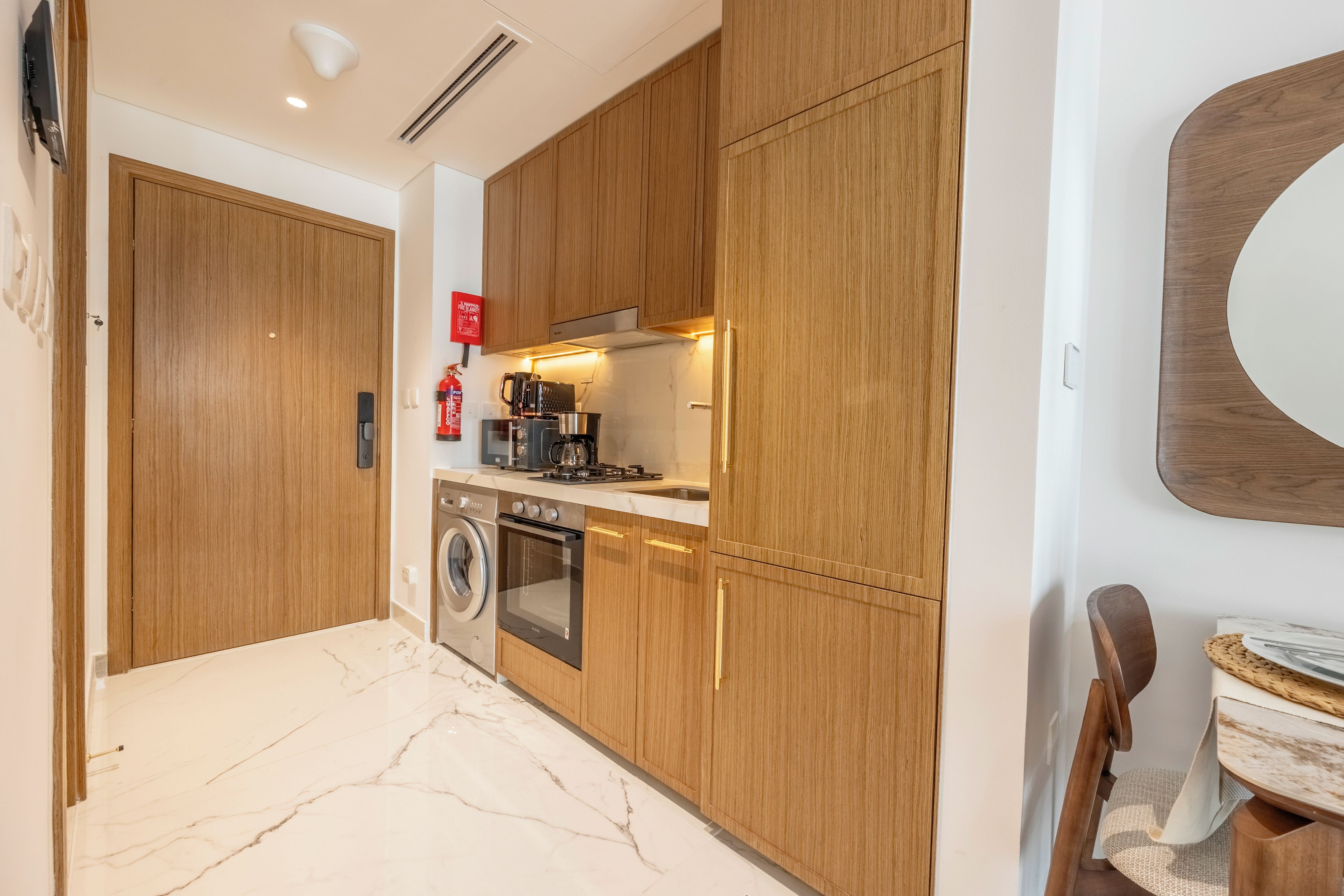 A modern kitchen with wooden cabinets, a built-in oven, a washing machine, and a coffee maker.