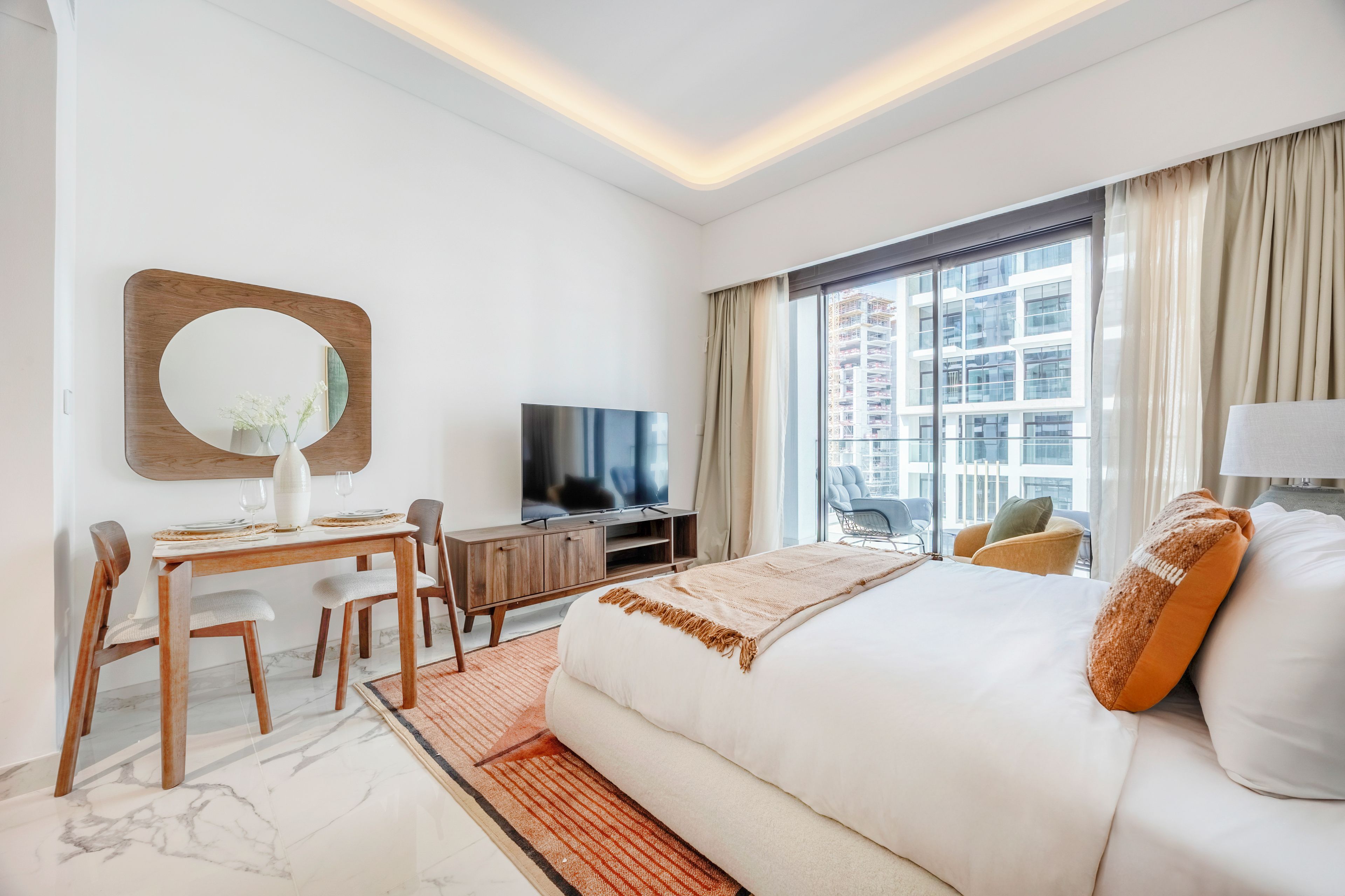 Habitación de hotel moderna con una cama grande, un escritorio con silla, televisor y vista a un paisaje urbano a través del ventanal.
